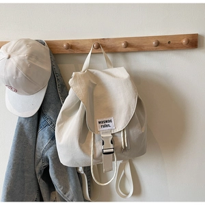 Detail of canvas backpack featuring silver buckle closure and woven label on white fabric