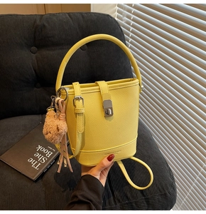 Détail du sac seau jaune grainé avec charm ours en peluche sur un canapé en velours