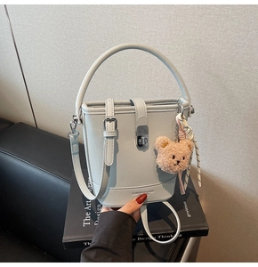 Vue détaillée du sac seau bleu clair en cuir grainé avec breloque ours et ruban élégant