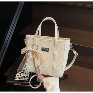 Detail of cream bucket bag with crocodile texture and lace bow on a wooden staircase