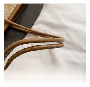 Détail de la poignée en cuir marron avec coutures fines sur un sac cabas en paille tressée