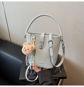 Détail du sac seau en cuir bleu clair à motif litchi avec marquage et bijou d'ours