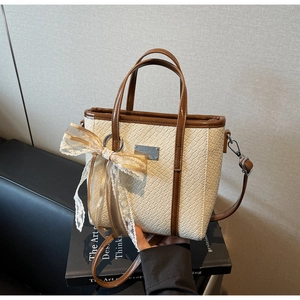 Dettaglio della borsa a secchiello beige coccodrillo con bordo marrone e fiocco pizzo