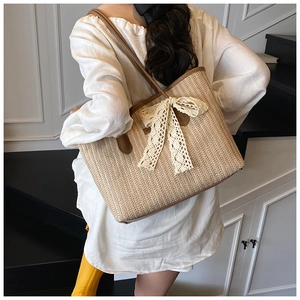 Détail du sac cabas en paille tissée avec nœud en dentelle blanche et anses brunes
