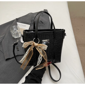 Dettaglio borsa a secchiello nera intrecciata con fiocco in pizzo e placca in metallo