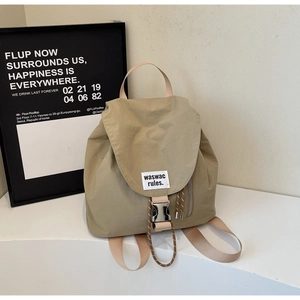 Detail of khaki nylon backpack featuring flip-top metal buckle and side zipper pocket