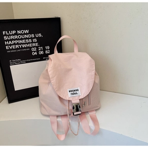 Close-up of light pink canvas backpack with black buckle closure and woven label