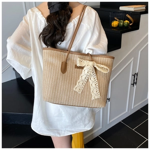 Détail d'un sac cabas en paille tressée beige avec un grand nœud en dentelle et anses en cuir