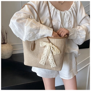 Détail d'un sac cabas en paille avec un grand nœud en dentelle blanche et anses en cuir brun