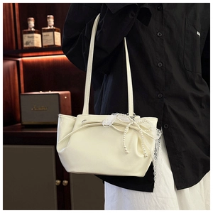 Détail d'un sac à bandoulière en cuir blanc avec nœud décoratif, perles et bordure dentelle