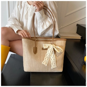 Détail du cabas en paille tressée avec nœud en dentelle beige et bandoulières en cuir brun