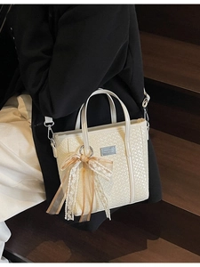 Elegant off-white woven tote bag with ribbon bow charm on dark wood background