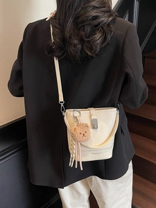 Sac seau chic en cuir crème avec breloque ours porté à l'épaule pour un look tendance