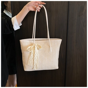 Détail d'un sac cabas tissé beige avec un nœud en dentelle et des anses en cuir
