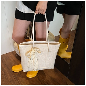 Détail d'un sac cabas tissé beige orné d'un élégant nœud en dentelle surdimensionné