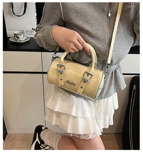 Detail of a light yellow cylinder handbag with glossy patent leather and silver hardware