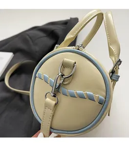 Detail of silver-tone metal hook and light blue woven trim on a cream barrel bag