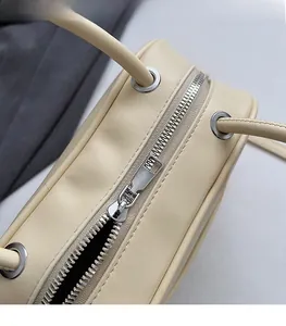 Detailed close-up of smooth silver metal zipper and leather texture on beige handbag