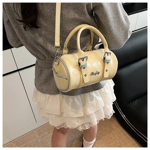 Detailed close-up of a light yellow cylindrical boston bag with blue trim and metal logo