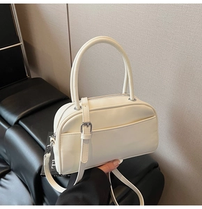 Detail of a creamy white Boston bag with elegant top handles and a metal zipper
