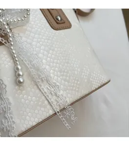 Detail der cremeweißen Beuteltasche mit Eidechsenprägung, Spitze und Perlenverzierung