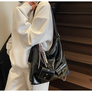 Détail d'un sac cabas en cuir synthétique noir brillant avec chaînes argentées sur un modèle