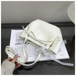 Détail d'un sac seau blanc cassé avec nœud, perles et rubans de dentelle