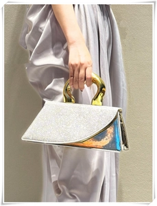 Detail of evening bag with white rhinestones, gold handle and holographic panels