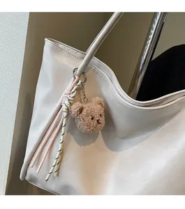 Brown teddy bear plush charm with woven lanyard and metal ring on cream tote bag