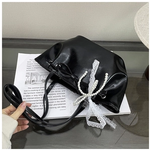 Détail du sac seau noir brillant avec de grandes perles et un nœud en dentelle blanche