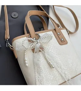 Detailansicht der weißen Schlangenleder-Beuteltasche mit Perlen-Schleifen-Anhänger auf grauem Mantel