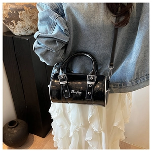 Close-up of a glossy black patent leather Boston bag with silver logo and buckle straps