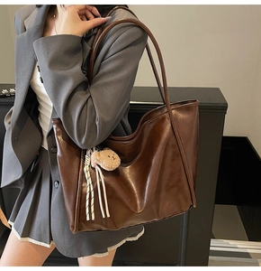 Detail of a brown leather tote bag featuring a cute teddy bear charm and striped ribbon bow