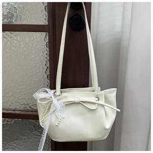 Détail du sac seau plissé blanc crème avec chaîne en perles et nœud sur une porte