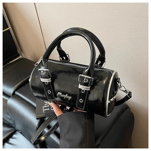 Detailed macro view of black patent leather cylinder bag with silver metal zipper and hardware