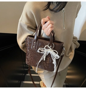 Detail der dunkelbraunen Eimer-Tasche mit Schlangenprägung und Perlen-Spitzenbogen