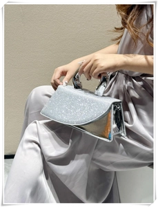 Detail of silver sequin handbag featuring a polished U-shaped metal handle and luxury shine