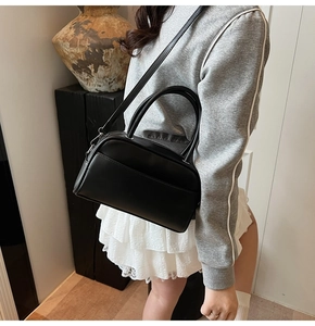 Detail view of black matte leather pillow bag with adjustable shoulder strap on a model