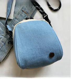Detailed top view of a light blue denim crossbody bag with dual zippers and strap