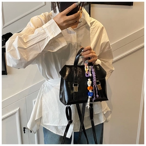 Close-up of black glossy handbag with metal buckle and colorful braided rope charms