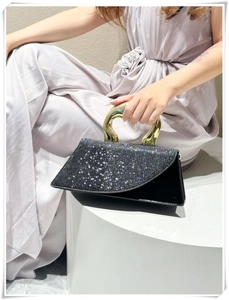 Detail of elegant black handbag featuring a golden metallic handle and sparkling glitter flap