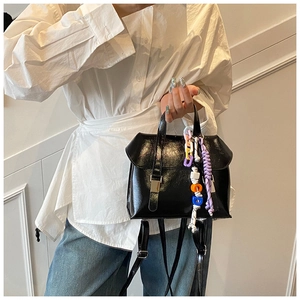 Detail view of a black shiny PU backpack with colorful chain charm and braided strap detail