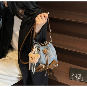 Detailansicht der blauen Denim-Beuteltasche mit braunem Lederbesatz und Bären-Anhänger