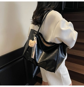 Detail of a black leather tote bag with a beige bear charm on a minimalist shoulder strap