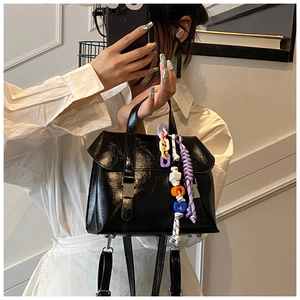 Detail of black glossy leather bucket bag with colorful chain strap and letter charm