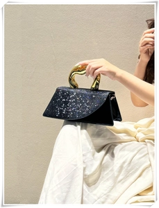 Detail of elegant black rhinestone evening bag with luxury gold wavy metal handle