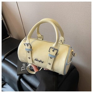Detail of light yellow cylinder handbag showing glossy patent leather texture and metal buckle