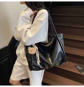 Detailed view of a black tote bag with a brown plush bear charm worn by a model