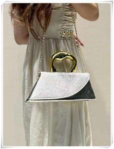 Close-up of glitter trapezoid handbag with gold organic handle and evening chain strap