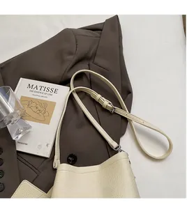 Detailed view of cream lychee leather bucket bag with adjustable strap on a brown blazer